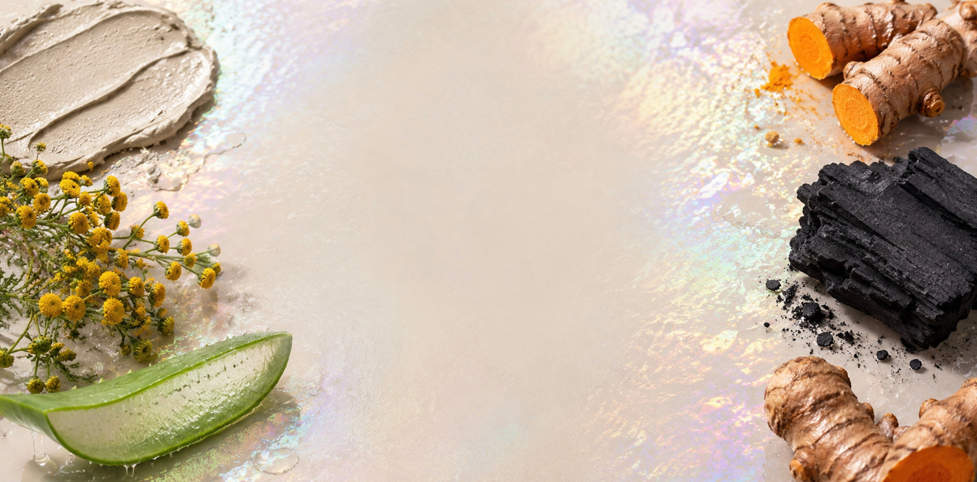 Strange ingredients including charcoal, turmeric, blue tansy flowers and aloe vera arranged around a soft pearlescent surface