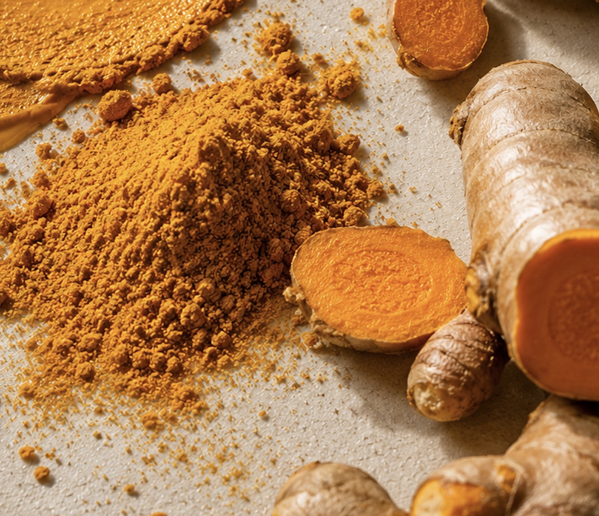 Fresh turmeric root sliced open beside a heap of gold turmeric powder